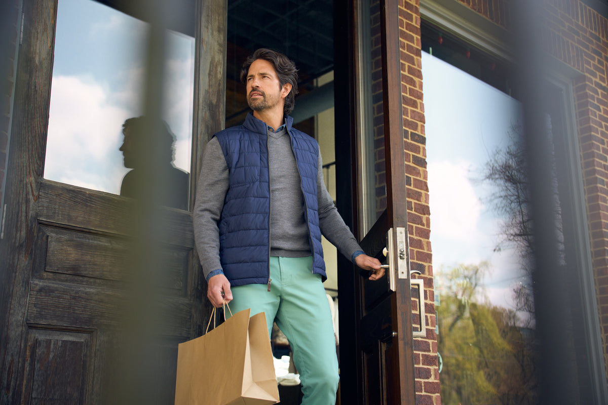 A man wearing a navy quilted vest and grey knit layer outside a storefront