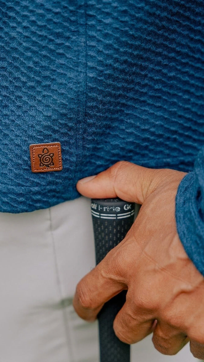 Blue Bellfield Hoodie texture and Turtleson patch, with a hand resting on a golf club